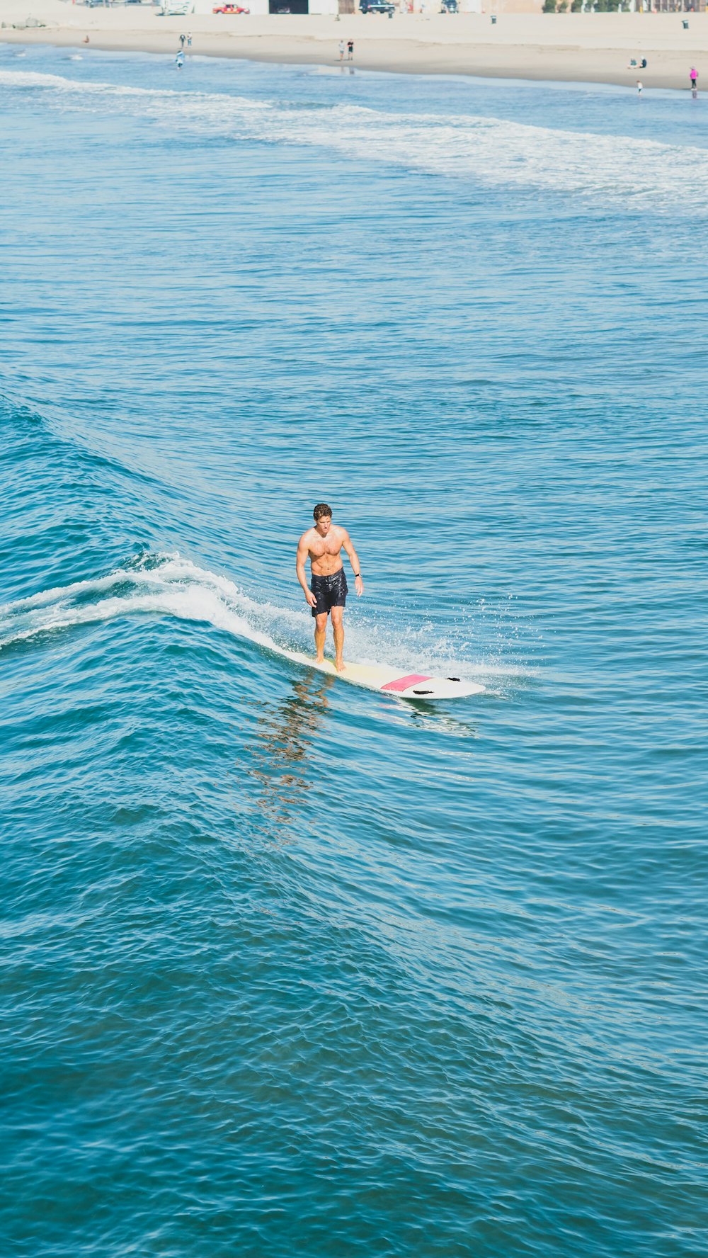 Frau im schwarzen Bikini steht tagsüber auf weißem Surfbrett auf blauem Meer
