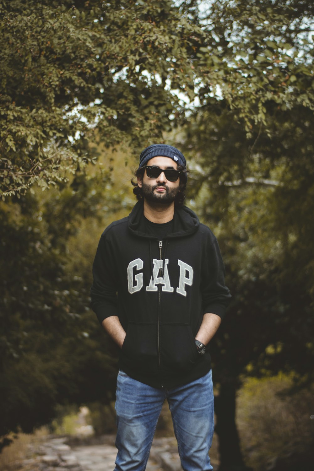 man in black and white nike hoodie wearing black sunglasses standing near green trees during daytime