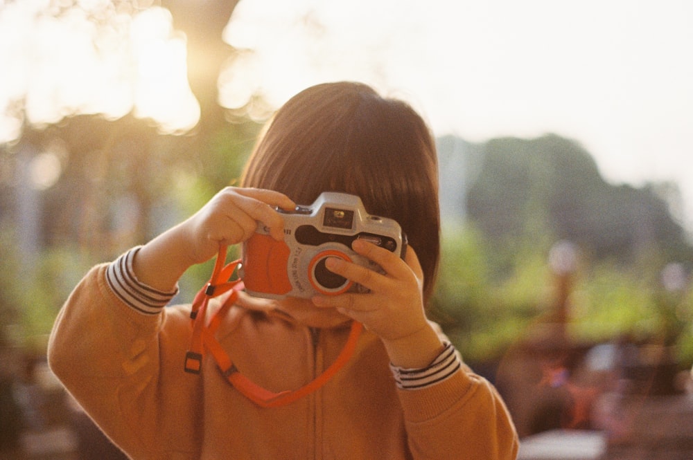 woman in orange jacket holding white camera