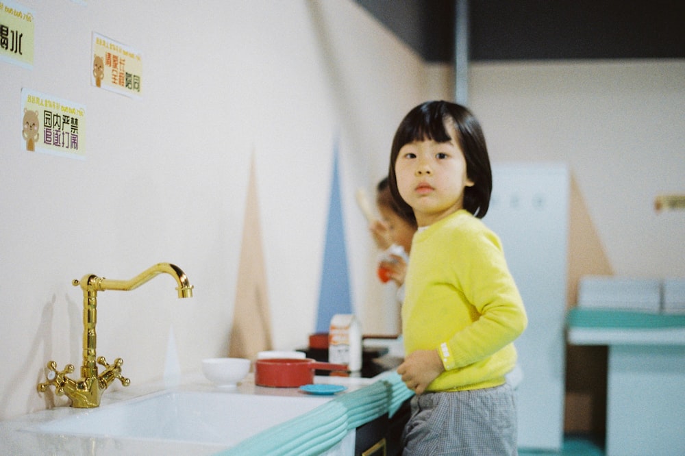 girl in yellow long sleeve shirt standing beside white ceramic sink