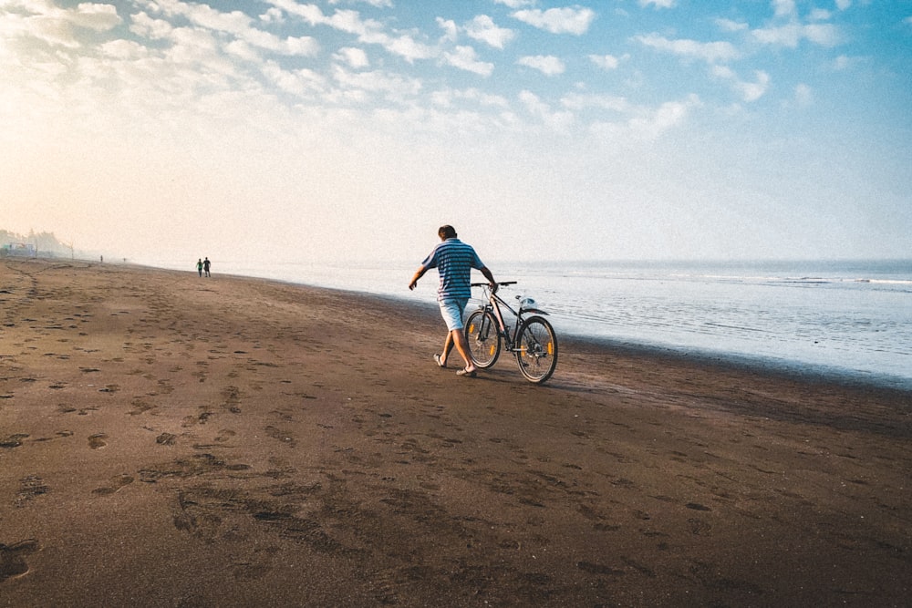 homme en chemise bleue faisant du vélo sur la plage pendant la journée