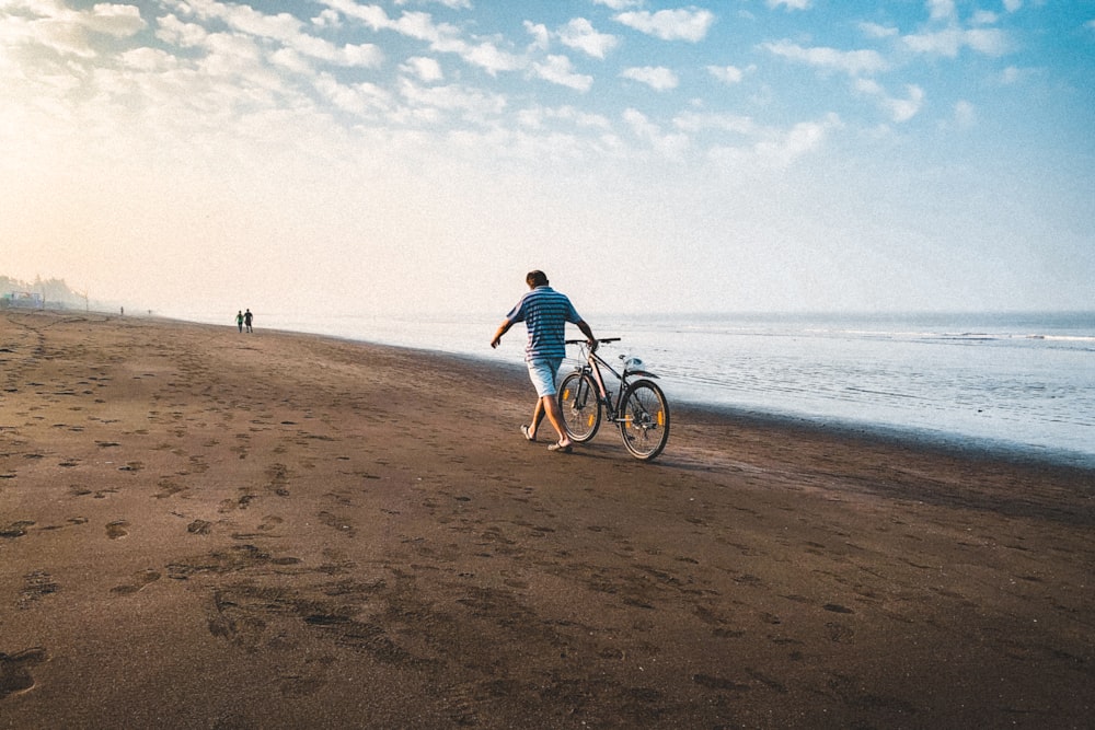 Mann im blauen Hemd fährt tagsüber am Strand Fahrrad