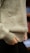 A close-up of a person wearing a light gray woolen sweater, with hands adjusting the bottom hem. The focus is on the texture of the sweater and the neutral colors.