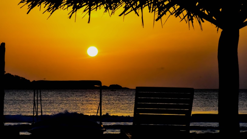 silhouette of bench near body of water during sunset