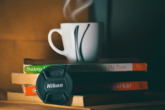 A stack of printed AI research papers next to a steaming mug labeled 'ai news'.