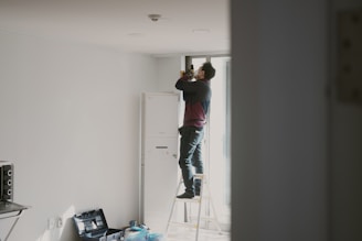 man in red shirt and blue denim jeans standing on white wooden door