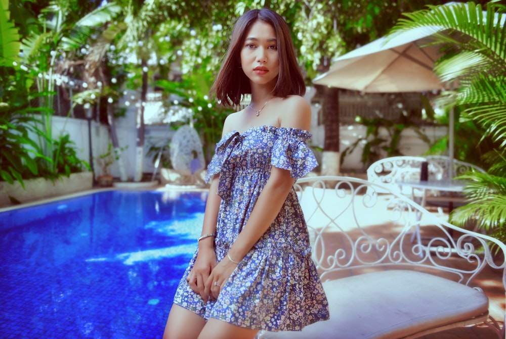 woman in black and white floral off shoulder dress standing near swimming pool during daytime
