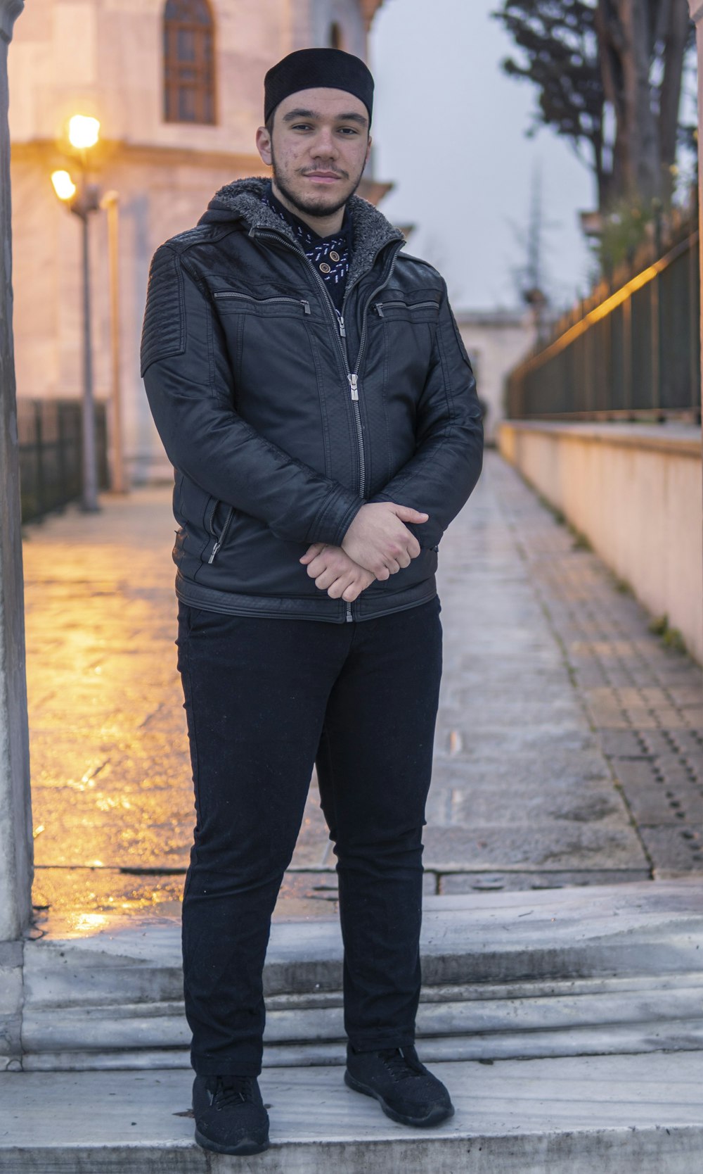 man in black zip up jacket and black pants standing on sidewalk during daytime