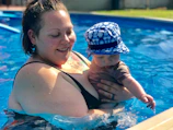 A parent gently holding their baby floating safely in a soft blue pool float.