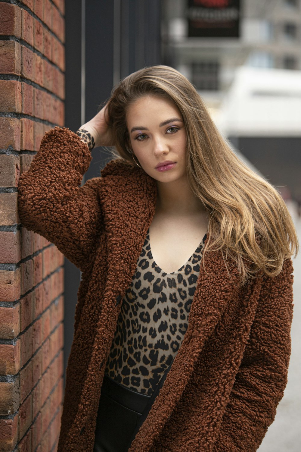 woman in brown and black leopard print long sleeve shirt leaning on brown brick wall