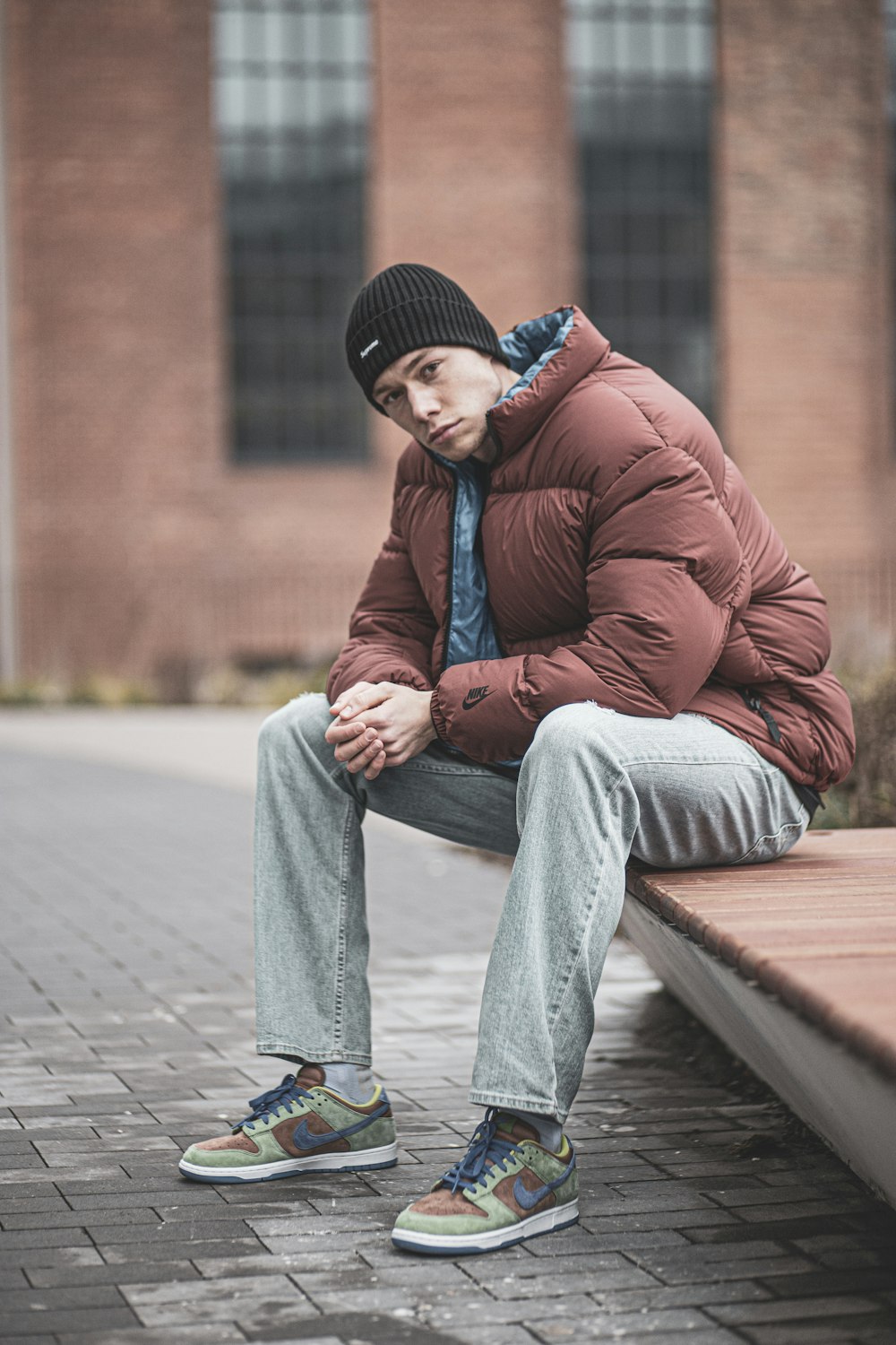 man in red jacket and gray pants sitting on brown wooden bench