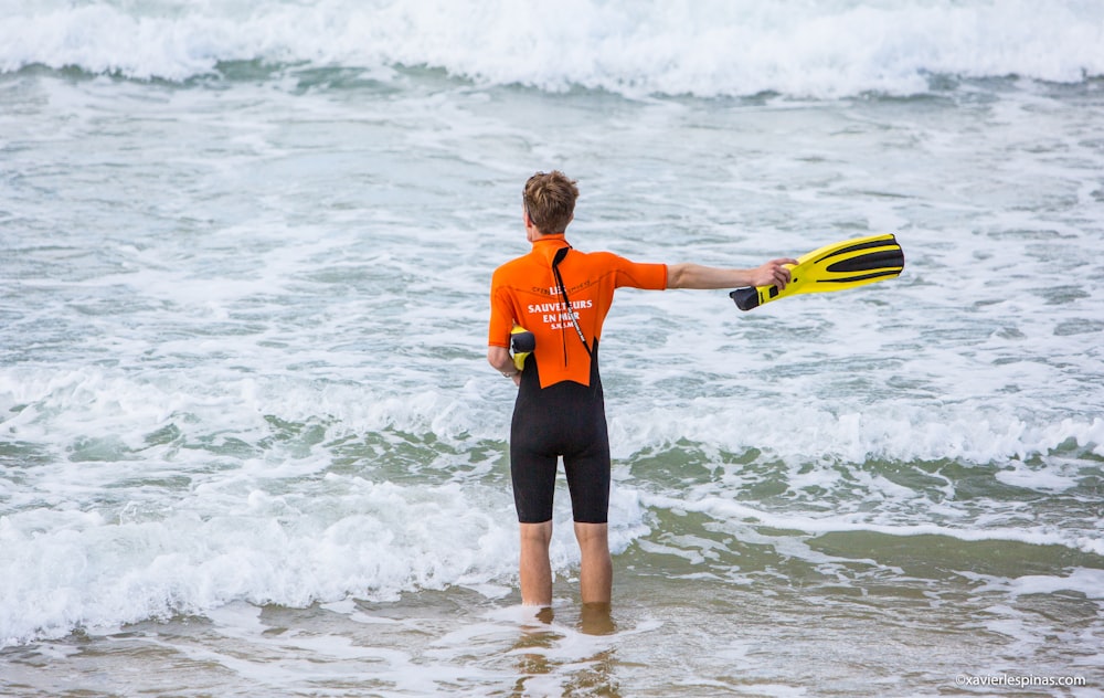 woman in orange and black wet suit holding yellow surfboard on sea during daytime
