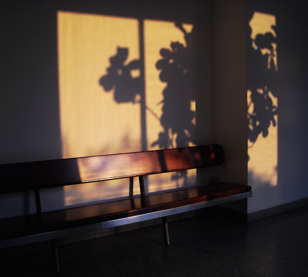 brown wooden bench beside white wall
