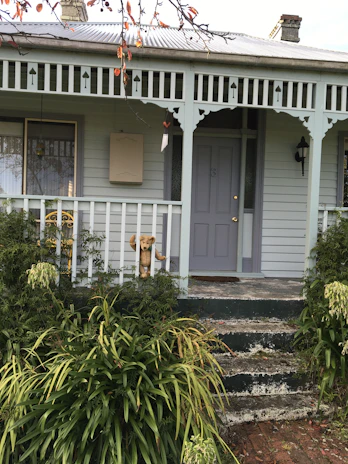 A whimsical dollhouse exterior with painted windows and a tiny porch garden.