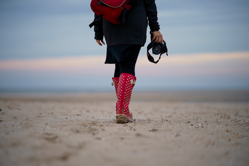 person in black jacket and red leather boots walking on beach during daytime