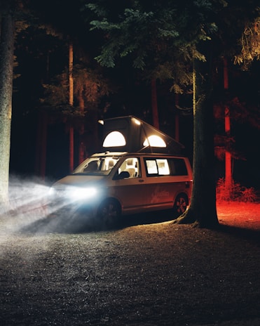 A cozy van parked in a forest clearing at sunset, with warm light glowing inside.