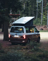 Happy family inside a camper van enjoying a picnic in a forest clearing.