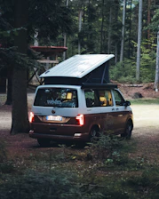 A sleek XGO Dynamic camper parked in a forest clearing at sunset, highlighting its elegant design.