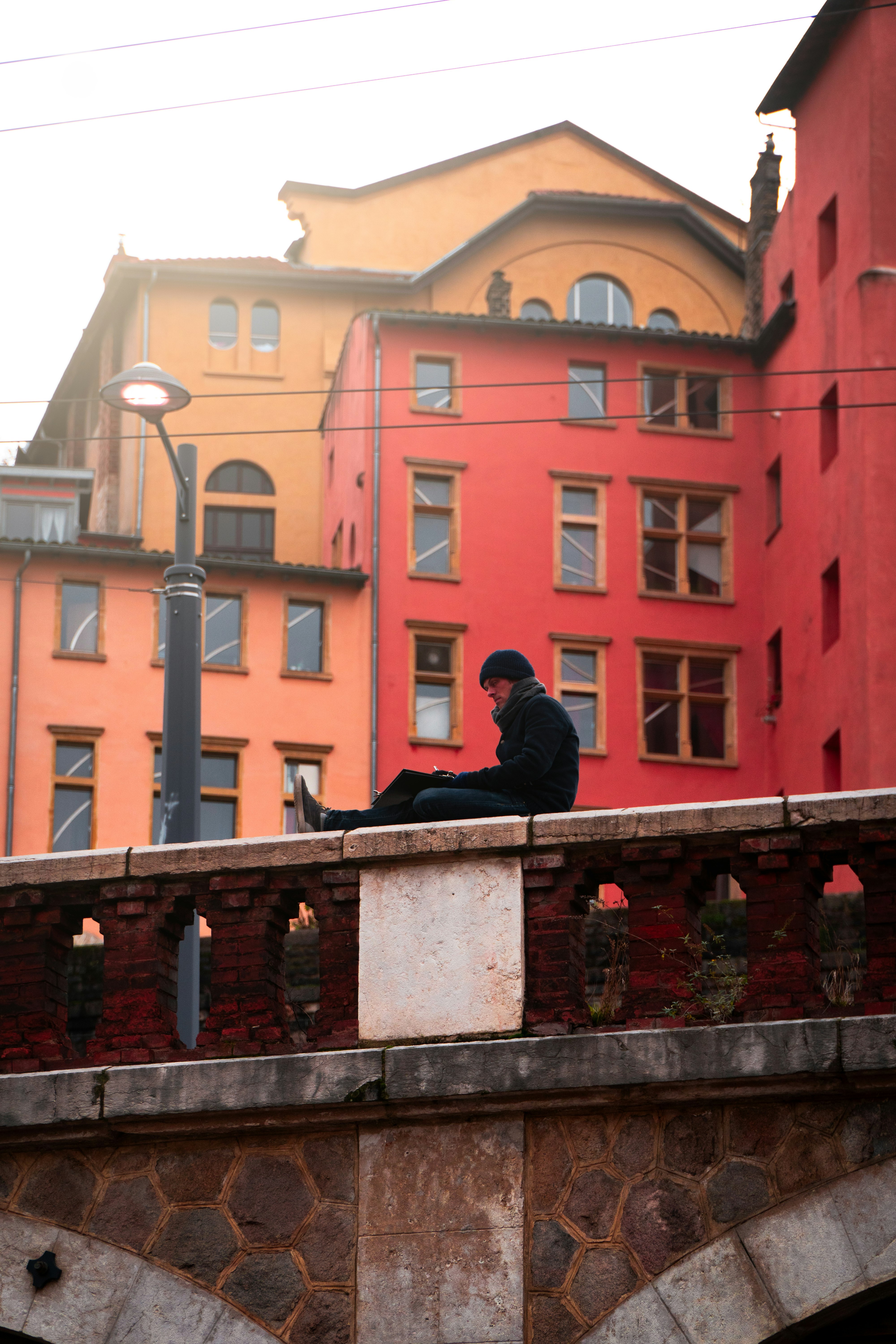 man in black jacket sitting on concrete bridge during daytime