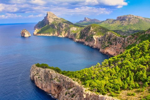 green and brown mountain beside blue sea under blue sky during daytime