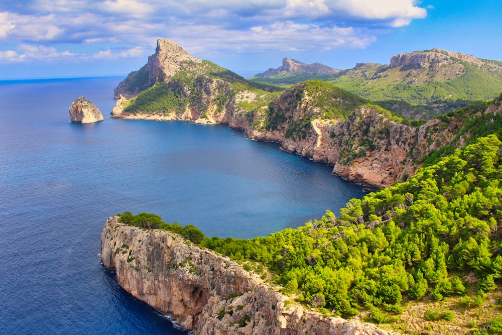 montagne verte et brune à côté de la mer bleue sous le ciel bleu pendant la journée