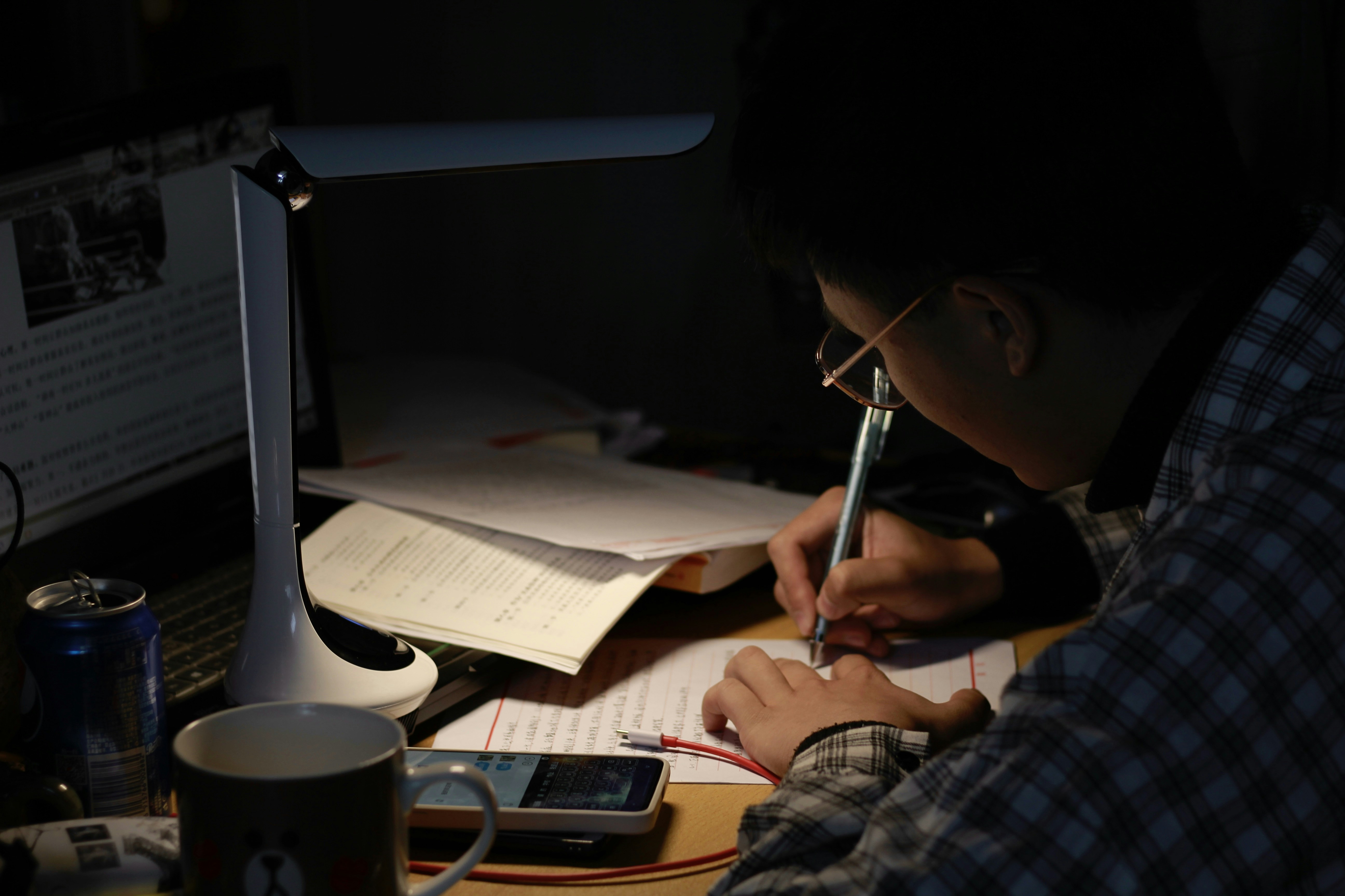 man in black and white plaid dress shirt writing on white paper, night work