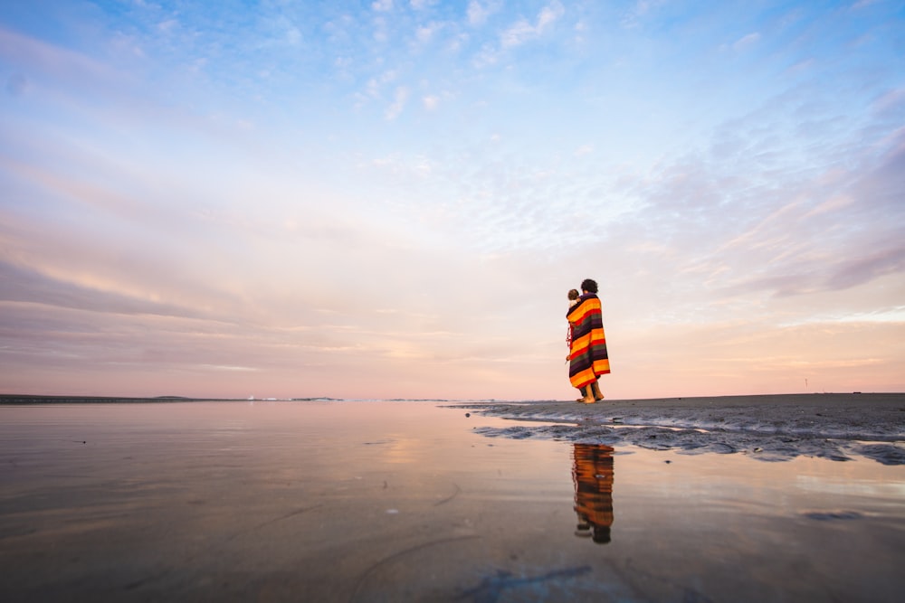 man in orange and white striped shirt standing on beach during daytime