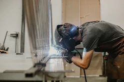 A skilled welder carefully working on a metal structure in a bright workshop.