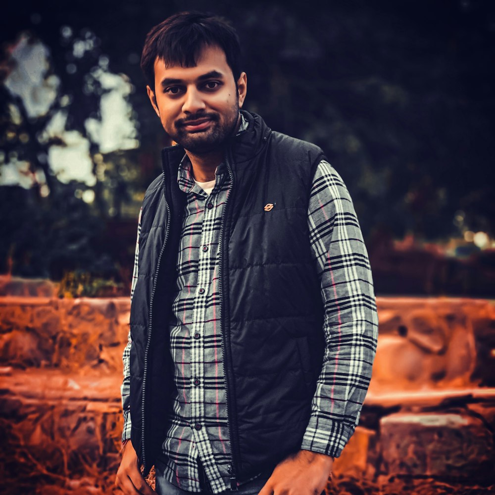 man in black and white plaid button up long sleeve shirt standing near brown rock