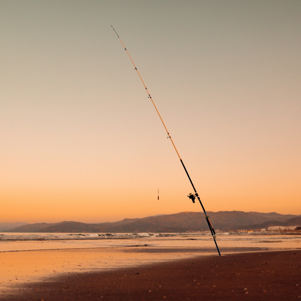black fishing rod on brown sand during sunset