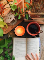 A candle burning gently beside an open book and a cup of tea.