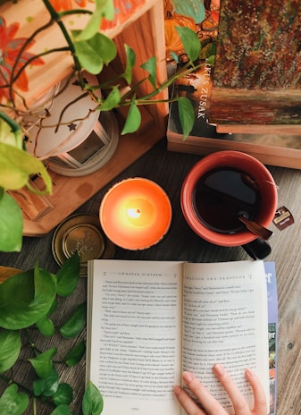 A cozy corner with a lit candle, a cup of herbal tea, and an open book about mindfulness on a wooden table.