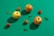 Three apples and several lychee fruits are artistically arranged on a vibrant green background. The apples have a warm, red and yellow hue, while the lychees appear rough-textured and reddish brown. Small sprigs of green mint leaves are scattered between the fruits, adding freshness and contrast.
