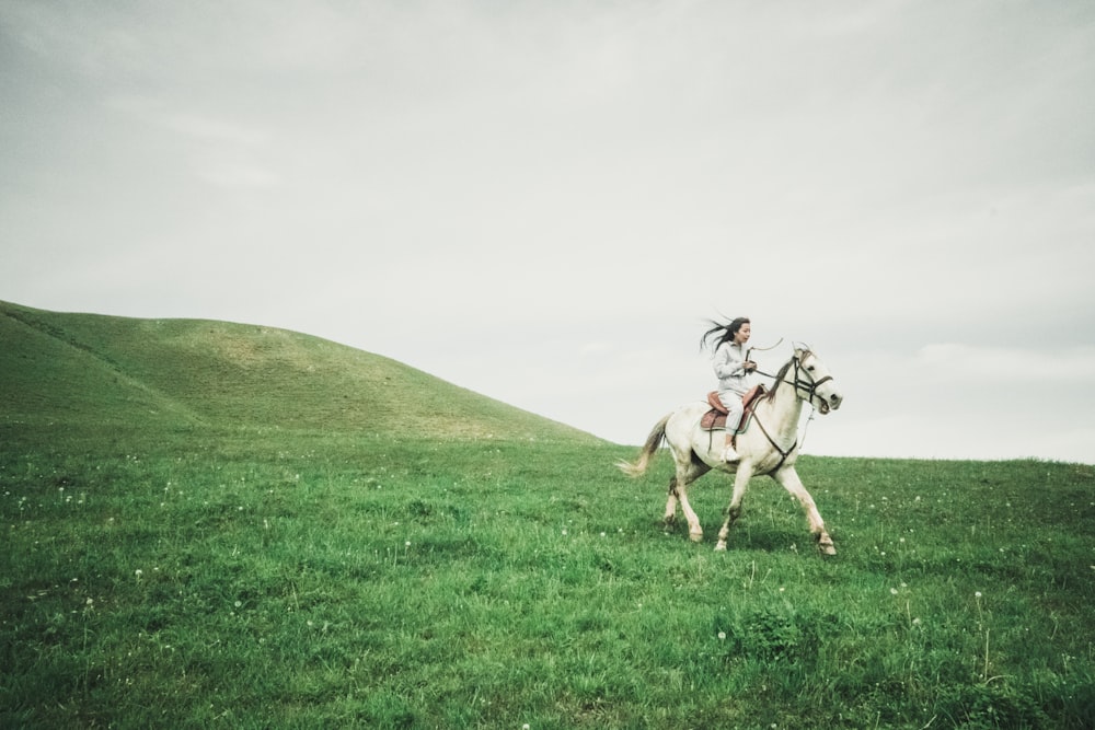 man riding horse on green grass field under white sky during daytime