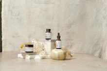 A minimalist arrangement of soft beige and buttery-toned beauty products on a clean, light background.