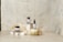 A minimalist arrangement featuring skincare products including a jar, a bottle with a dropper, and another jar. These items are placed on white blocks, accompanied by delicate dried flowers and a decorative stone object. The background is a textured, light-colored surface that enhances the serene and natural aesthetic.