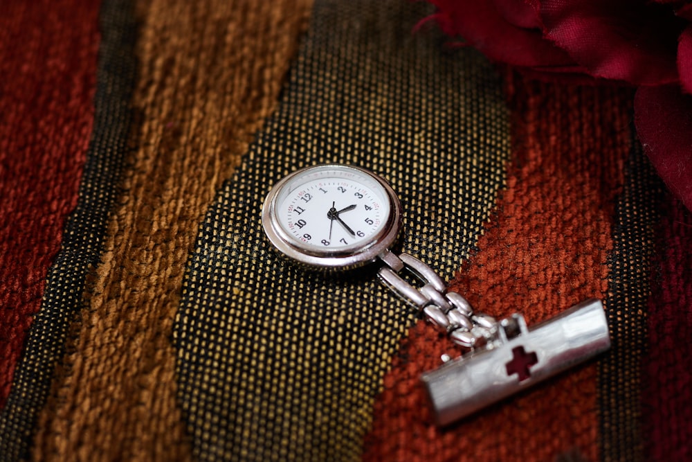 silver pocket watch on brown textile