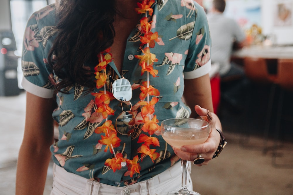 woman in blue red and green floral shirt holding clear drinking glass