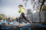 woman in green tank top and black leggings doing yoga on blue round trampoline