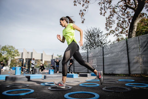 woman in green tank top and black leggings doing yoga on blue round trampoline