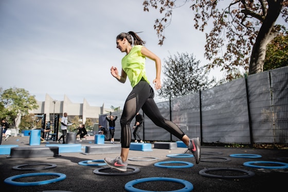 woman in green tank top and black leggings doing yoga on blue round trampoline