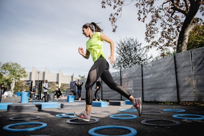woman in green tank top and black leggings doing yoga on blue round trampoline