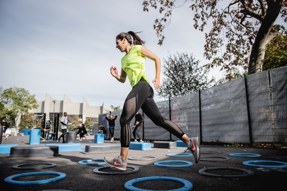 Mujer con camiseta verde sin mangas y polainas negras haciendo yoga en trampolín redondo azul