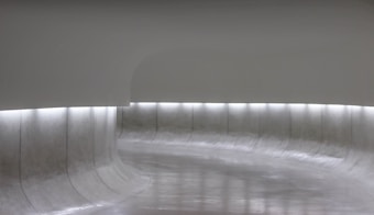 A minimalist, curved space with smooth, grey surfaces and soft lighting. The low, horizontal illumination runs along the walls, creating a serene and futuristic atmosphere.