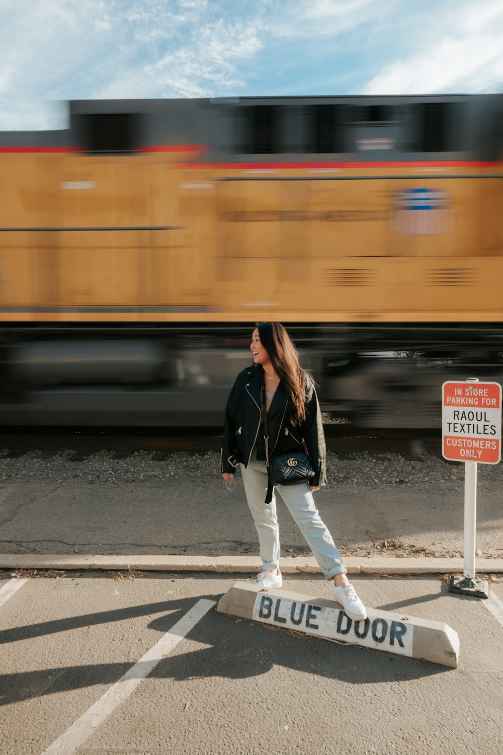 woman in black leather jacket and white pants standing on pedestrian lane during daytime