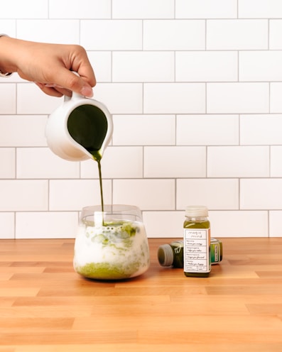 person pouring green liquid on clear drinking glass