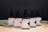 A row of five brown glass dropper bottles, each labeled with 'Batch' and featuring different geometric designs. The labels indicate various CBD concentrations with product names like 'Original' and 'Calm'. The background is a dark shade, while dried palm leaves are arranged at the base.