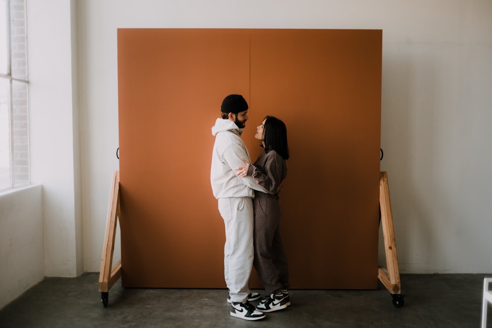 man and woman kissing in front of brown wall