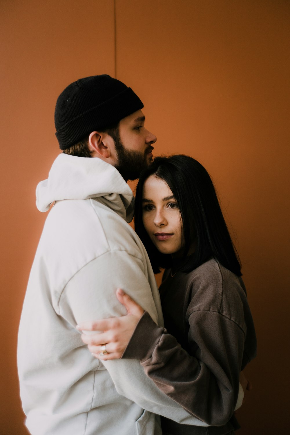 man in white hoodie hugging woman in black knit cap