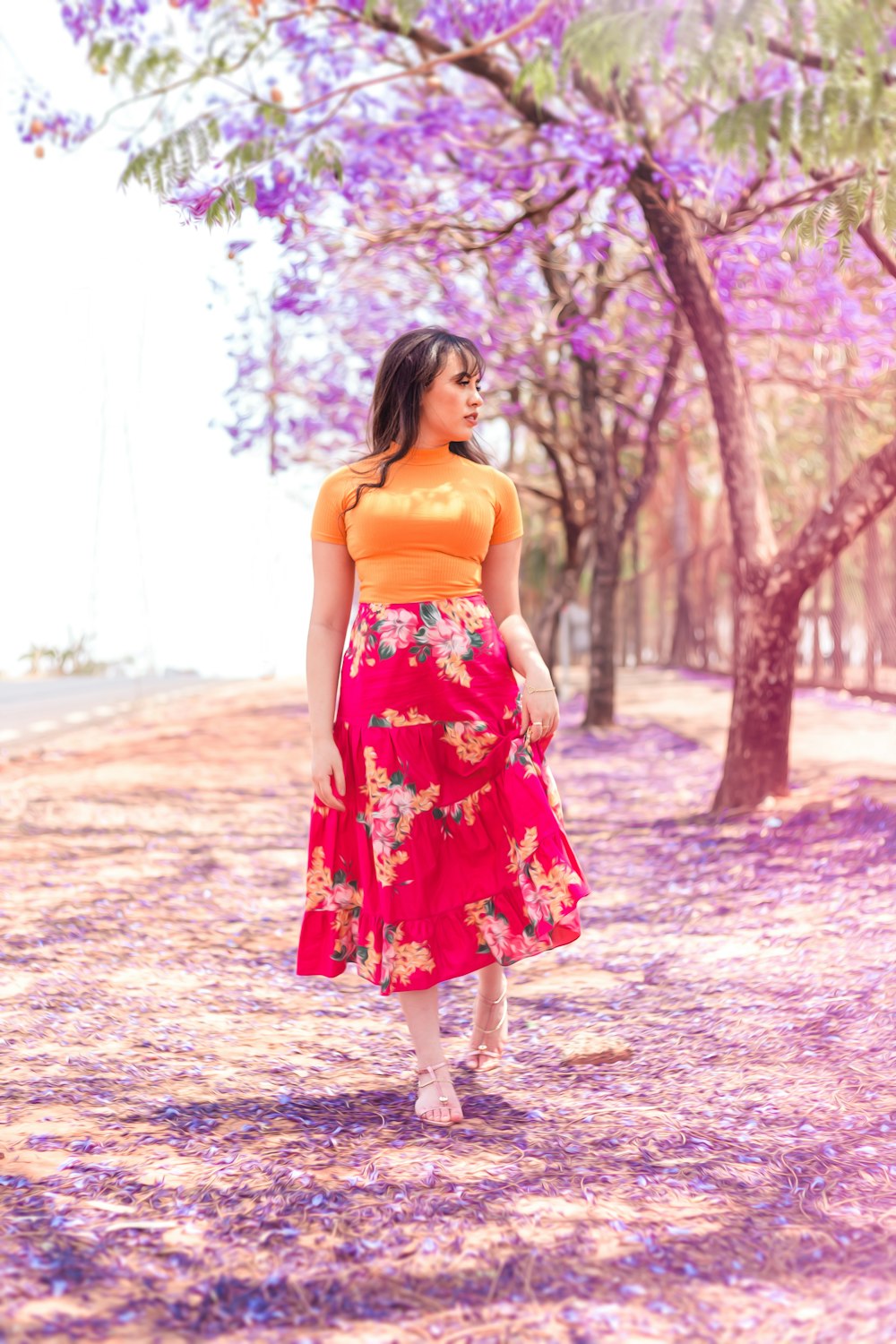 woman in red and white floral spaghetti strap dress standing on purple leaves during daytime